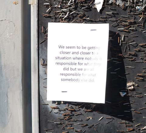 stapled to a notice board on the sidewalk is text graffiti with words about responsibility