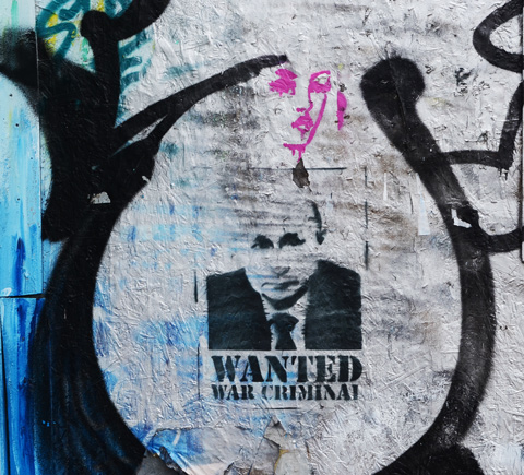 two stencils on hoardings, one is a pink woman's head and the other is a wanted poster for putin, war criminal, Russian leader for his invasion of ukraine