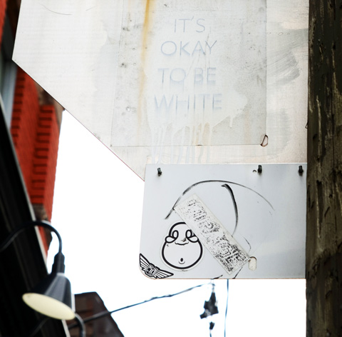 on the back of street traffic signs, two slaps. On top is one with words It's okay to be white, and on the bottom a small face with a round surprised mouth
