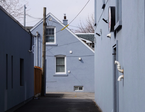 looking down a short alley to a pale grey side of a house, same grey as building on north side of alley