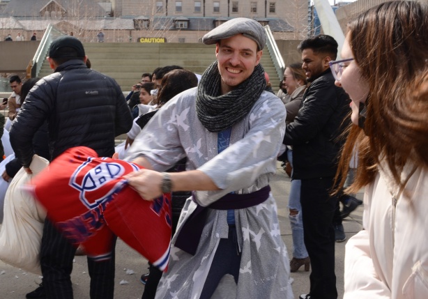 people participating in pillow at nathan phillips square, outdoors, fighting with pillows, man in a bathrobe and beret, fighting with a pillow with Montreal Canadiens pillow case