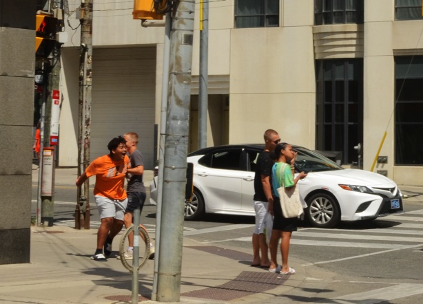 a person in orange t shirt and white shorts running to cross intersection of Bay and College
