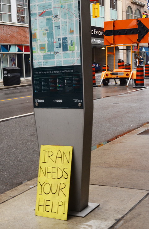 hand written sign on ground leaning against an information and map stand on Yonge Street, poster says Iran needs help
