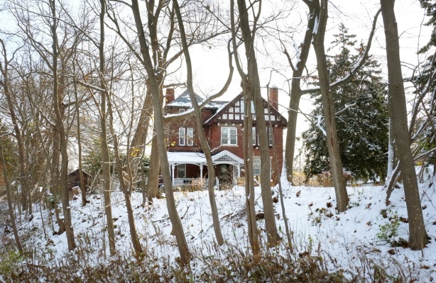 old two storey brick house on a hill surrounded by large trees, in the snow