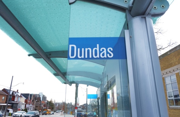 looking through the top of a TTC bus shelter with blue sign for Dundas, Lansdowne Ave in the backgound