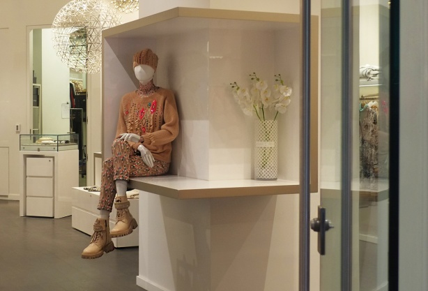 in a store, looking in the door, a faceless mannequin sits on a counter with legs crossed, 