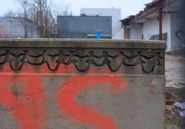 view of part of a demolition site, concrete half wall with decorated top, looks like carved dancing people 