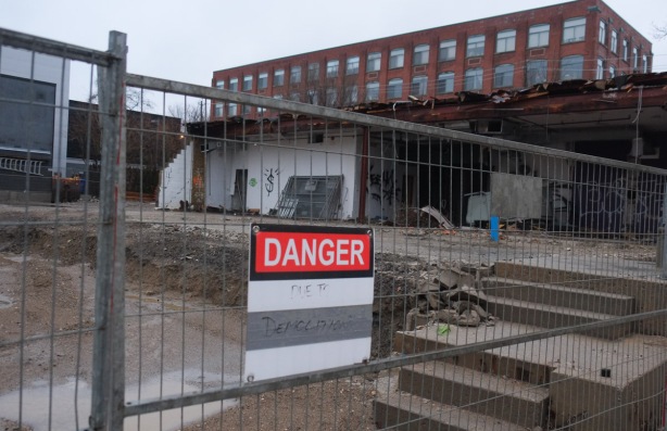 danger due to demolition sign on a fence at a construction site. partially demolished building on the site along with muddy land