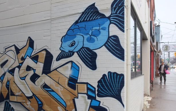 part of a painting on the side of a store, a blue fish and some lotus leaves