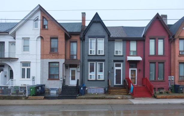 bay and gable row houses on gerrard street, painted in different colours, grey, white, maroon, one with a bright red staircase and railing. 