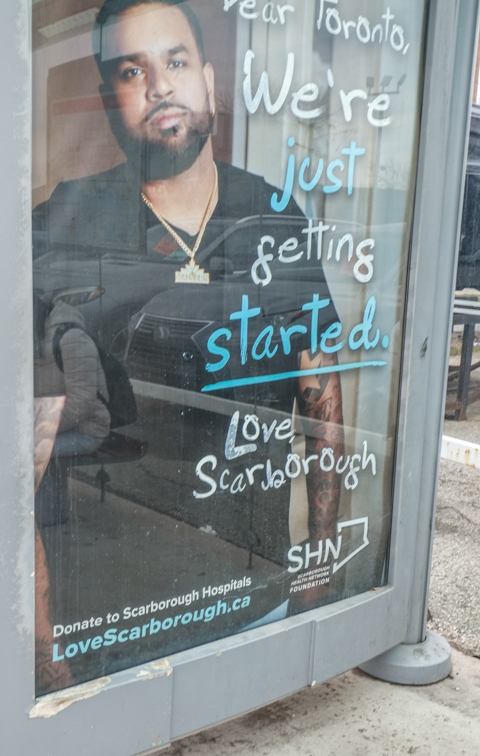 advertisement in a bus shelter for Scarborough Hospital, photo of a black man in scrubs, with text that says dear toronto, we're just getting started, love scarborough