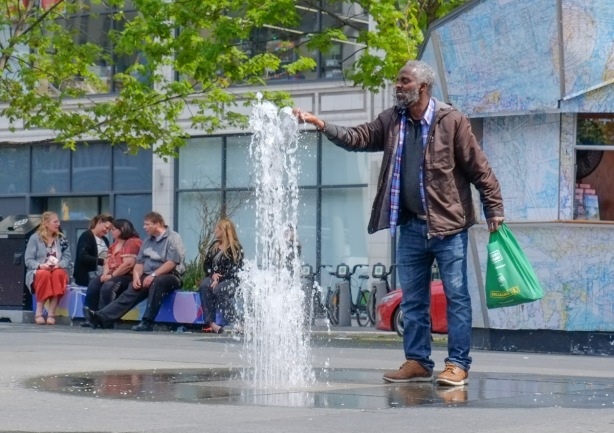 an older black man is sticking his hand in a fountain at Yonge and Dundas