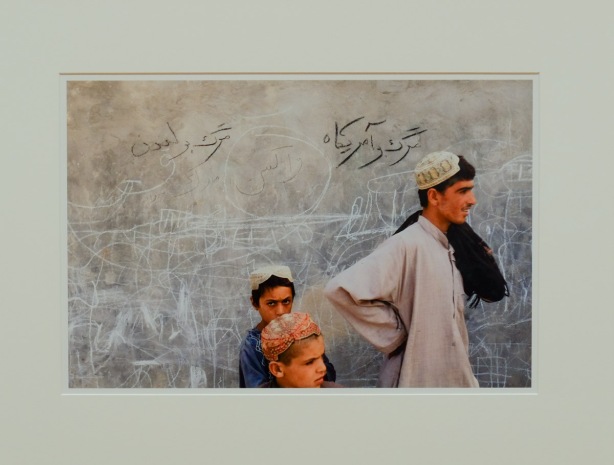 photograph in a gallery, three young men, one is looking at camera, Arab clothing, 