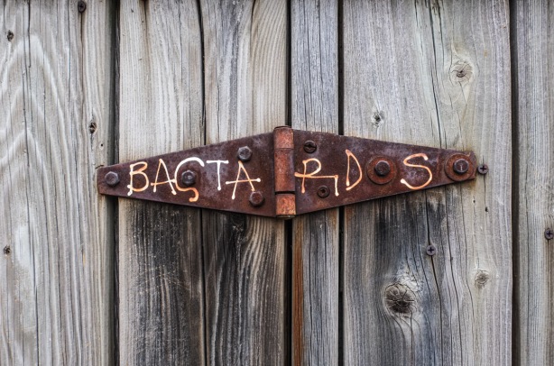 rusty hinge on wood gate, with word bastards scratched into the metal