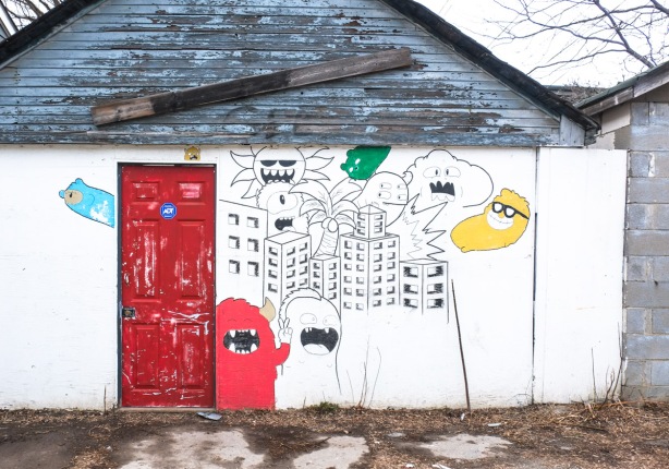 white garage in an alley, with a red man door, drawing and painting on the wall 