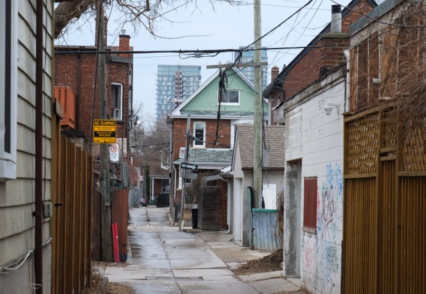 looking down a toronto alley, no dumping sign, garages, back of brick house, glass and steel highrise condo in the background