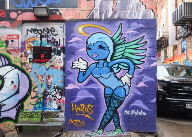 tuffytats painting on a wall in graffiti alley, female figure in purple with wings and a halo