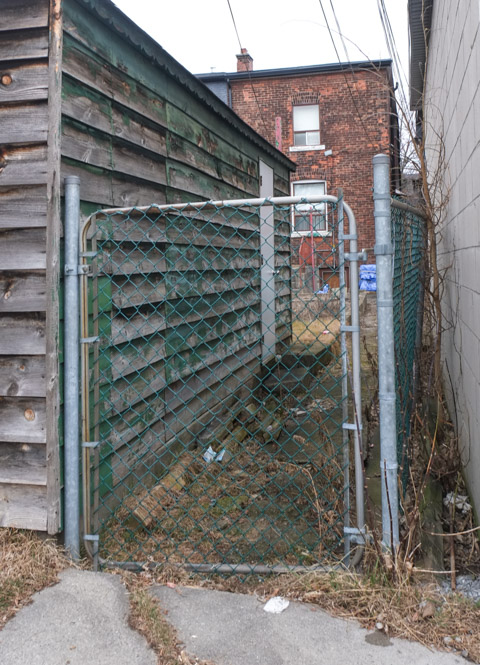 chainlink gate between two garages in an alley, with view into backyard