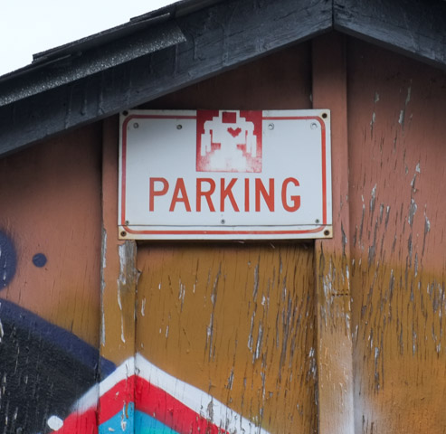 an old red and white lovebot sticker on a no parking sign on a garage in an alley