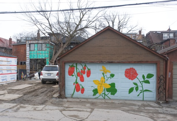 a simple mural of flowers on a garage door in an alley, with house next door under renovations