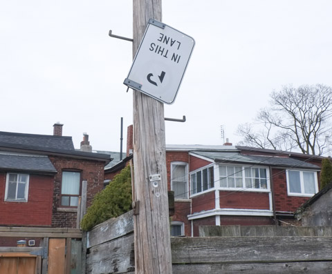 upside down street sign that says no parking in the alley, backs of houses in the background