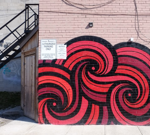 street art on side of white brick building, red and black swirls