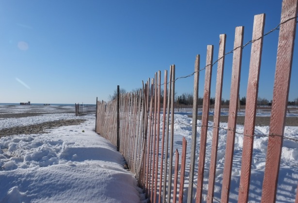 faded orange wood snow fence in winter, at the beach