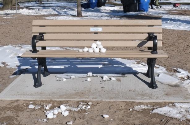 a pile of snowballs left on a wood bench at the beach