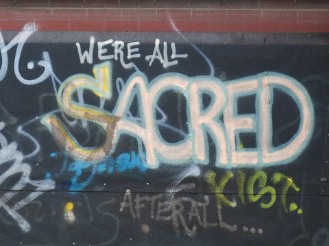 words scrawled on a wall that say we are all sacred