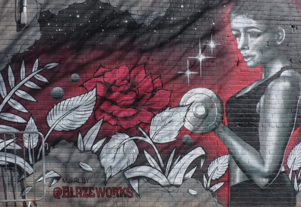 mural by blazeworks, a young woman lifting hand weights, a red rose, other white leaves