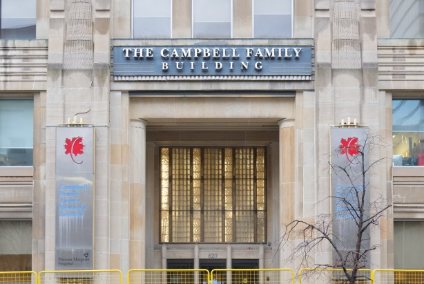 front door of Campbell Family Building, an old stone building with large decorative glass rectangle above the door, but behind yellow construction fence because of work being done on University Avenue