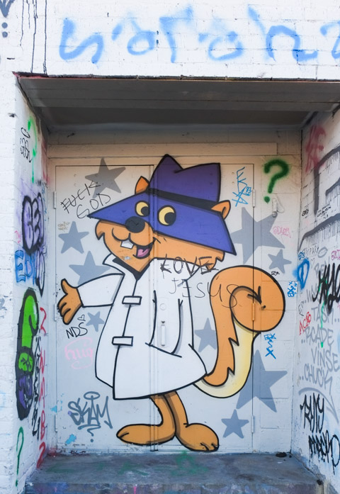 cat cartoon character, with purple hat over its eyes, white trench coat, mural in a doorway in an alley