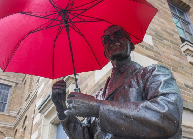 statue of a man, bronze, holding a real red umbrella