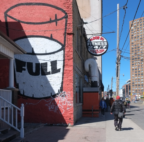 large painting of a glass half full of milk, on exterior of red building, word full written on the milk, beside Bloor Street fitness, with a large white boxing glove outside