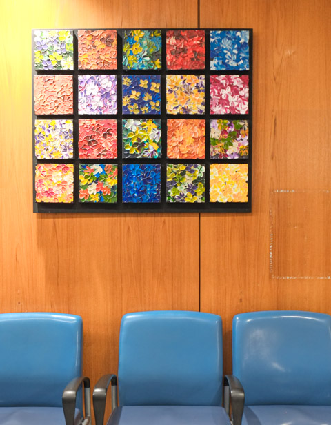 artwork on wood paneled wall and above three blue chairs