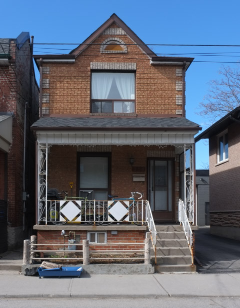 older brick two storey single family home with single upper storey window, also a porch across the front of the house, with white metal railing on porch