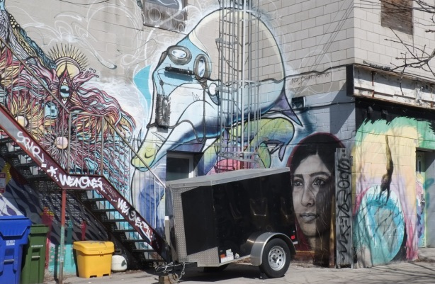 trailer parked in font of walls covered with street art murals including a woman's portrait by jarus
