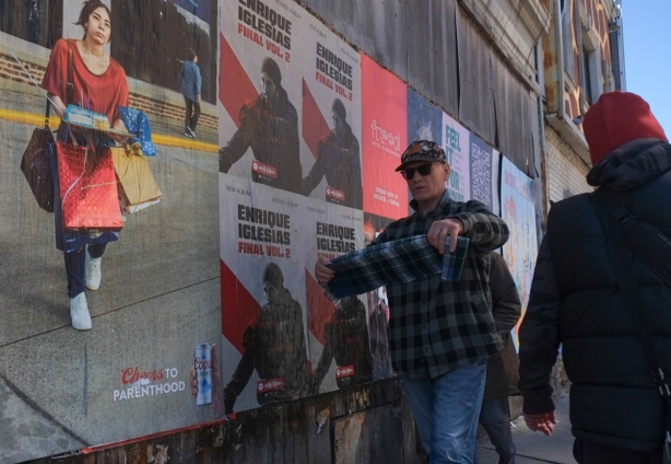 man holds a piece of plaid fabric in his outstretched arms as he walks past advertisements on exterior of giraffe building