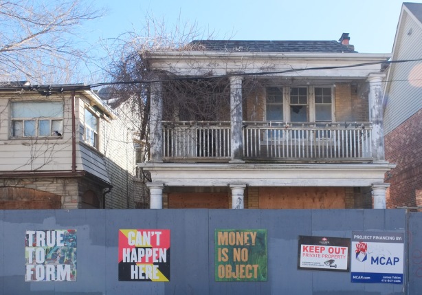 blue plywood hoardings with signs on them, large house behind the hoardings with balcony on upper level