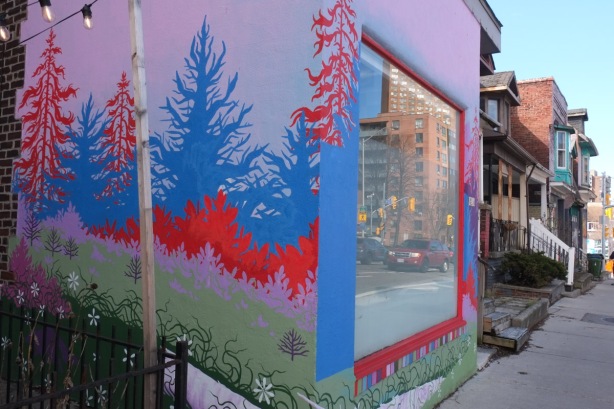 addition to front of house, extends to sidewalk, large window in front, with reflections, walls are painted in mural with purple sky, blue and red trees, and green grass