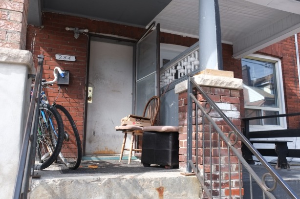chair on a porch with 3 pizza boxes on it, also a bike on the porch