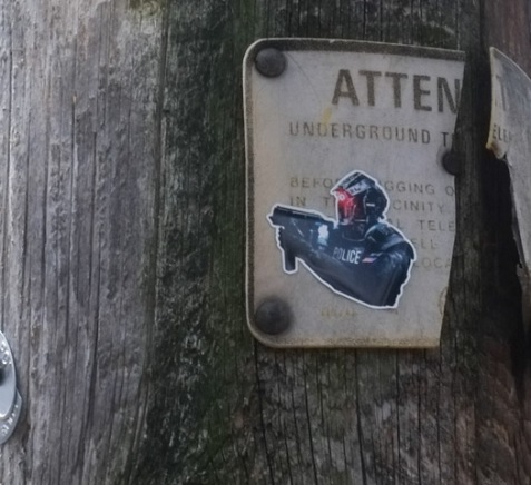 sticker of a heavily armed police man with a large gun on a pole in an alley