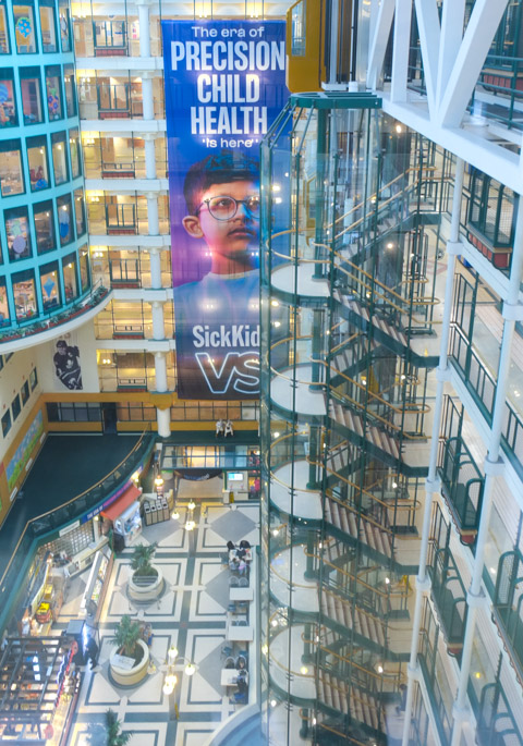 large multi storey atrium of Sick kids hospital, with elevator and stairs and window to rooms on the sides 