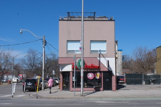 two story building with a Tim Hortons, pale pink building, no buildings on either side of it, a woman in a pink coat walks past