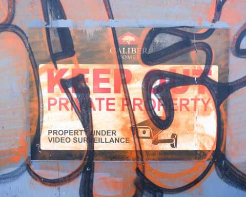 sign that says keep out private property under video surveillance has had orange spray paint sprayed on it 