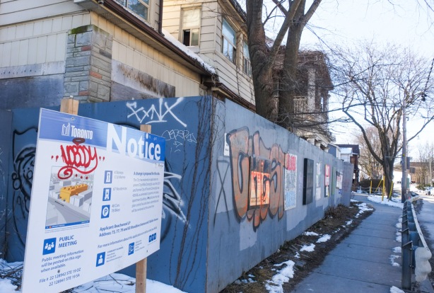 city of toronto notice of development in front of a row of empty houses with blue hoardings in front, sidewalk, a couple of trees, 